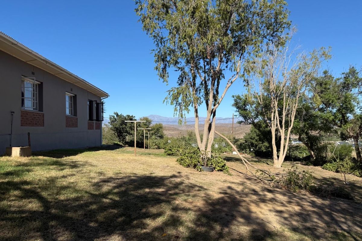 Rear view of the property showing the side facade, lawn area, and established trees with mountain views in the background.