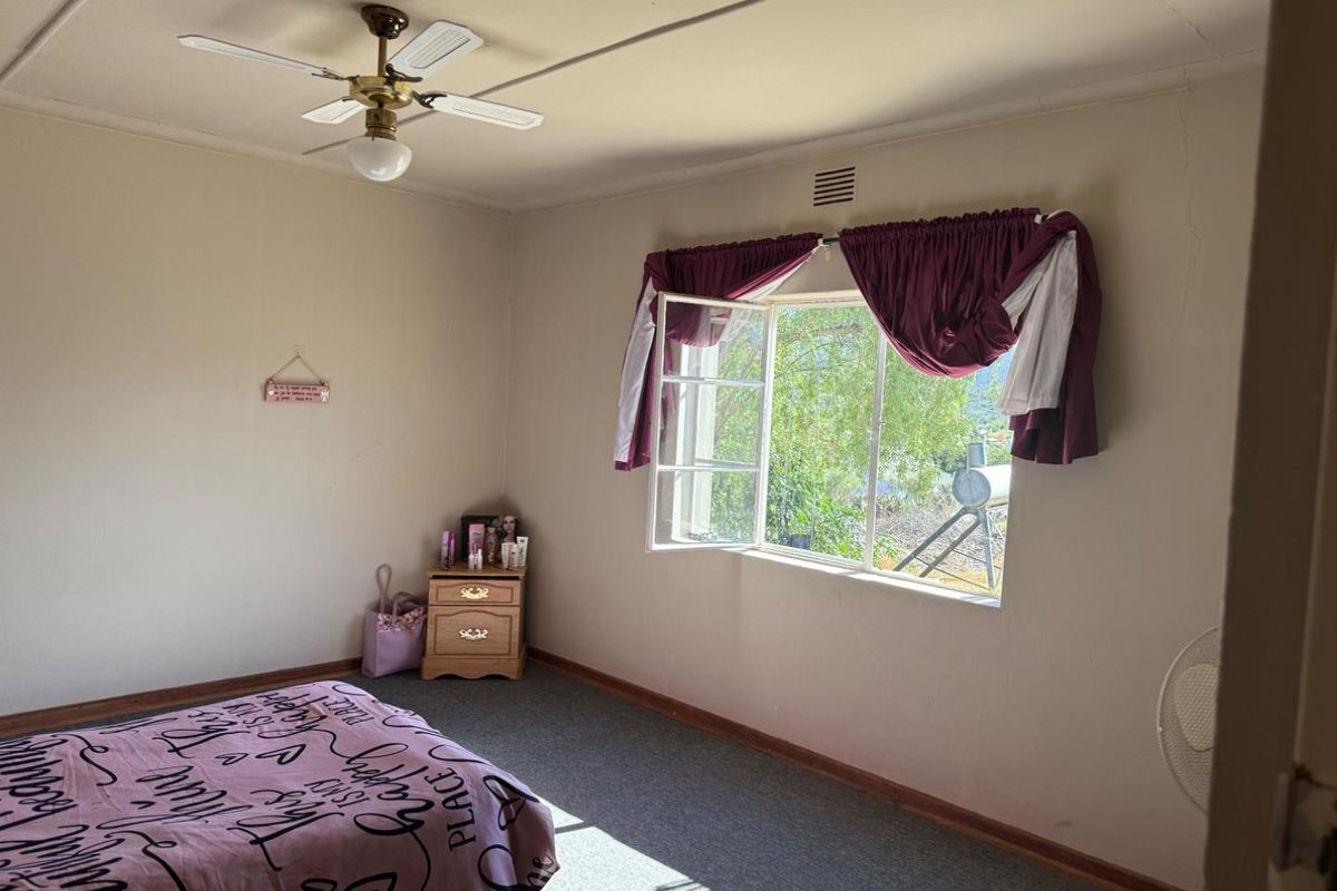 A bedroom featuring a ceiling fan, casement window, and ventilation grille, showing signs of wear on the wall surfaces.
