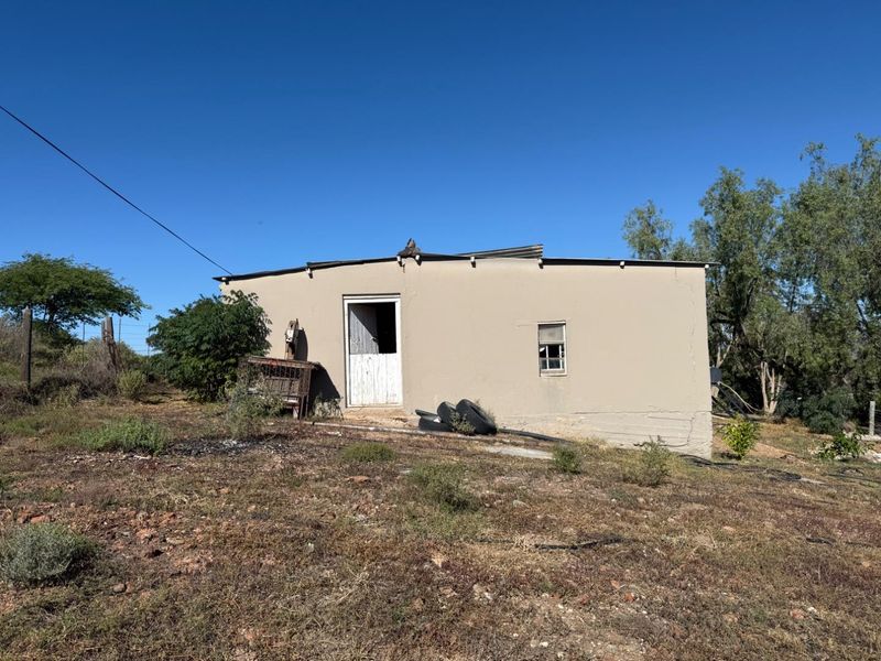 A detached single-story structure featuring a corrugated metal roof and weathered exterior walls, situated on a rural plot.