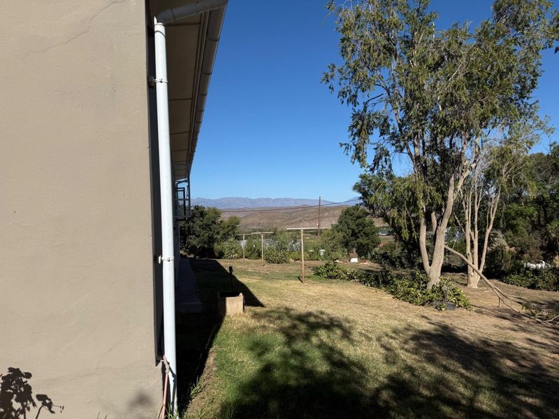 A view of the rear garden and lawn area, featuring established trees and a scenic mountain backdrop.