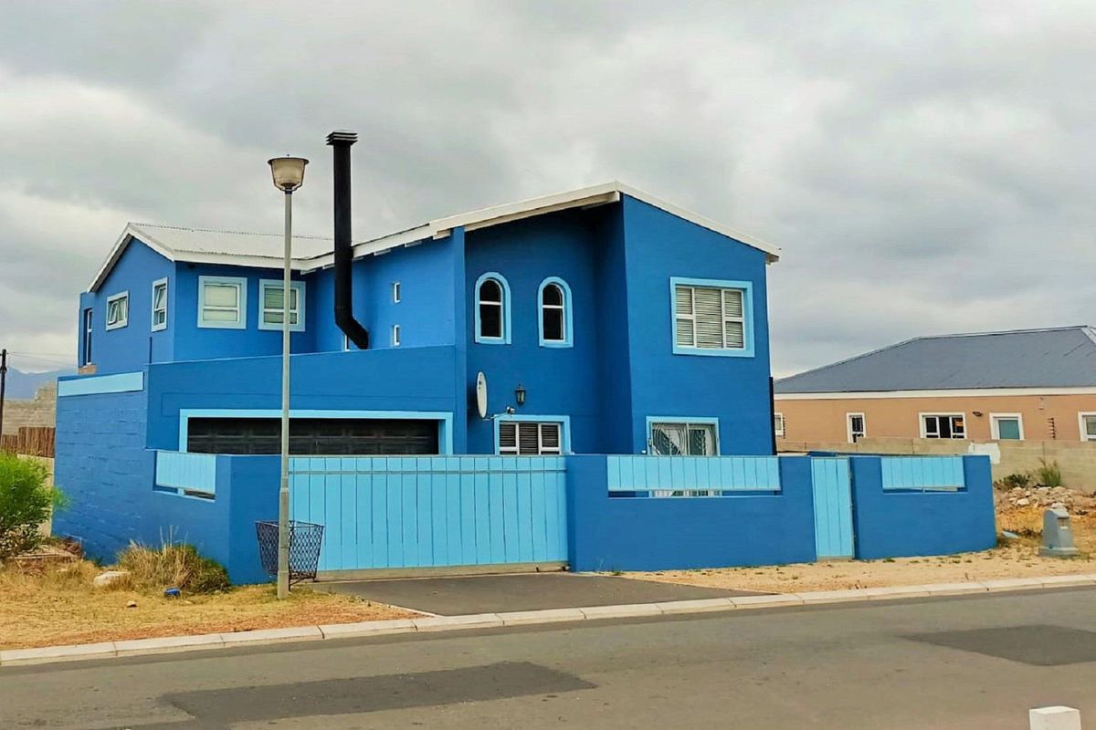A two-story detached house featuring a bright blue exterior facade, a metal roof, and a matching blue perimeter boundary wall with a gate.