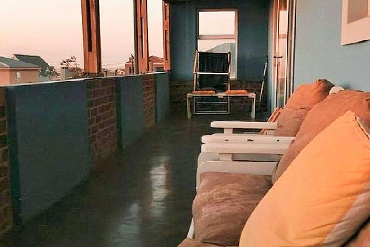 A covered balcony featuring exposed brick and painted wall sections, polished concrete flooring, and an open-air design overlooking the surrounding neighborhood.