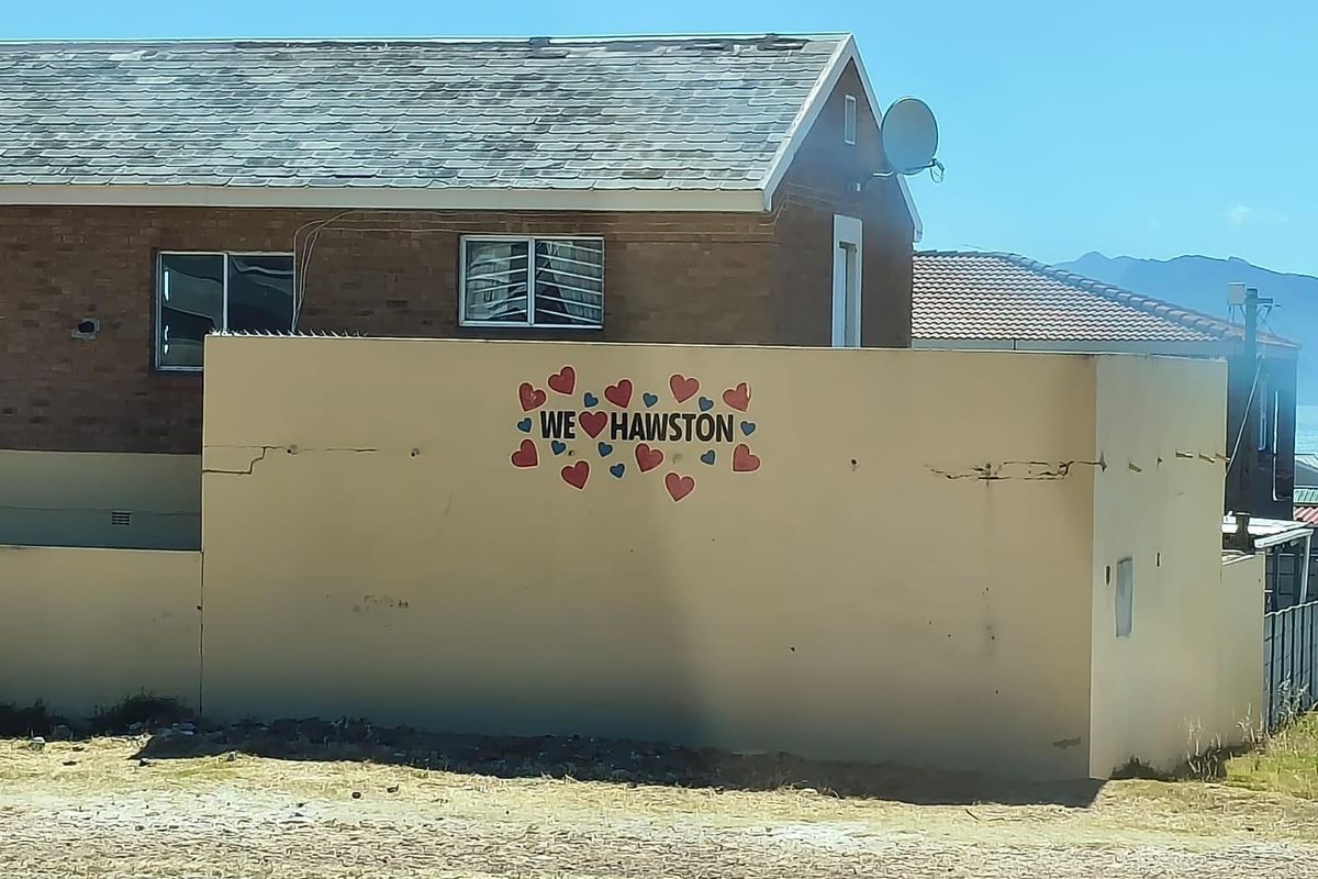 Exterior view of a brick house featuring a prominent boundary wall with decorative heart mural and visible structural cracking.