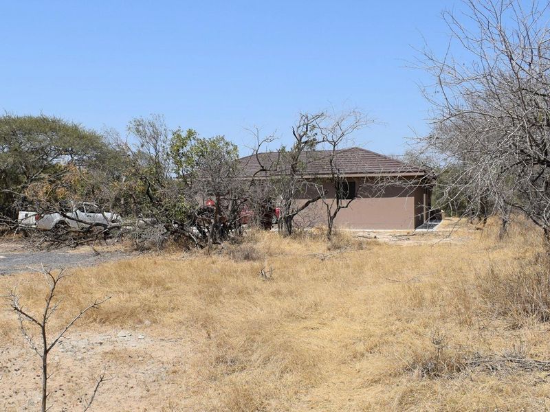 A view of the front exterior of a single-story house with a hipped roof, situated on a dry, natural bushveld plot.