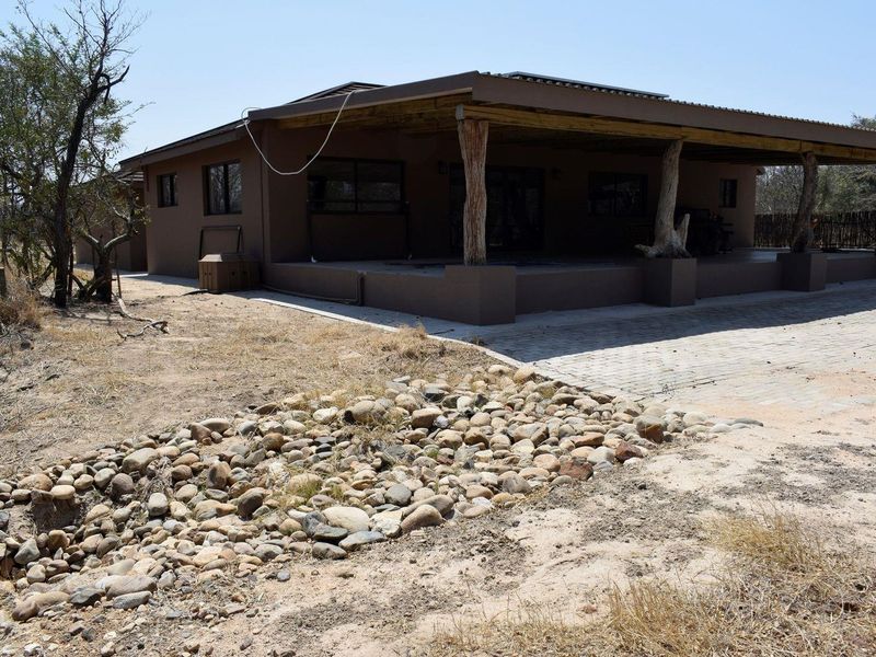 Rear view of the property featuring a large covered patio area with timber support posts and a paved driveway section.