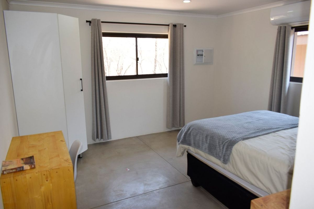 A clean, modern bedroom featuring polished concrete floors, a wall-mounted split-system air conditioner, and neutral finishes.