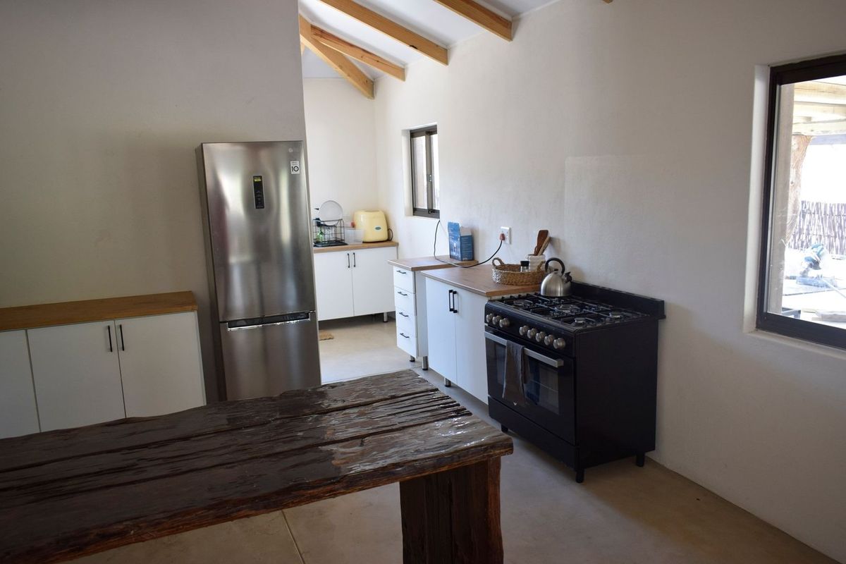 A bright kitchen featuring white cabinetry, wooden countertops, a gas stove, and exposed timber ceiling beams, offering a clean and functional workspace.