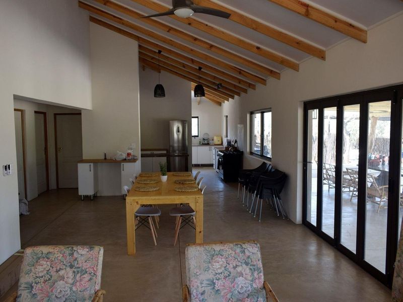 Spacious open-plan living and dining area featuring exposed timber rafters, polished concrete floors, and large bi-fold doors opening to the outdoor space.