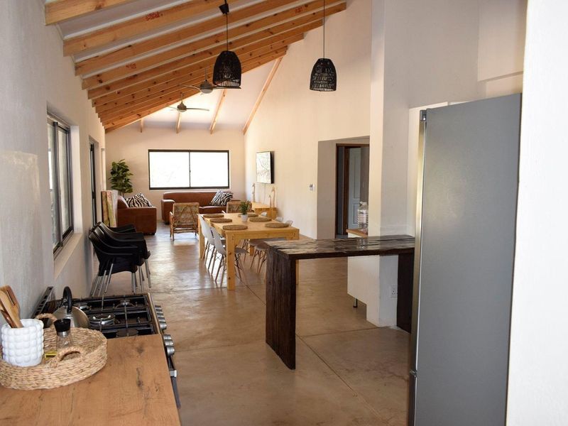 Spacious open-plan living and dining area featuring high vaulted ceilings with exposed timber rafters, polished concrete floors, and a functional kitchen with breakfast bar.