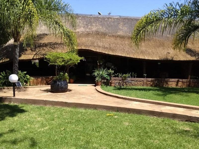 Front view of a farm-style property featuring a traditional thatched roof, a paved entrance walkway, and a well-maintained garden area.