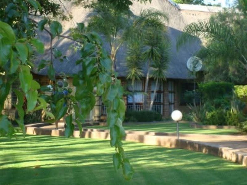 A view of the rear garden featuring a well-maintained lawn, paved pathways, and the exterior facade of a thatched-roof farm property.