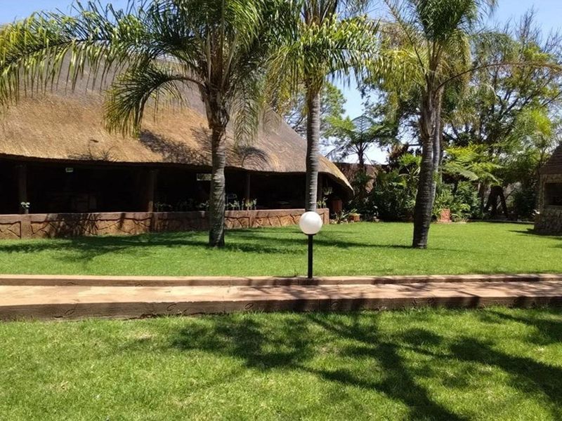 A well-maintained garden area featuring a thatched roof structure, a stone-clad outdoor fireplace, and established palm trees.
