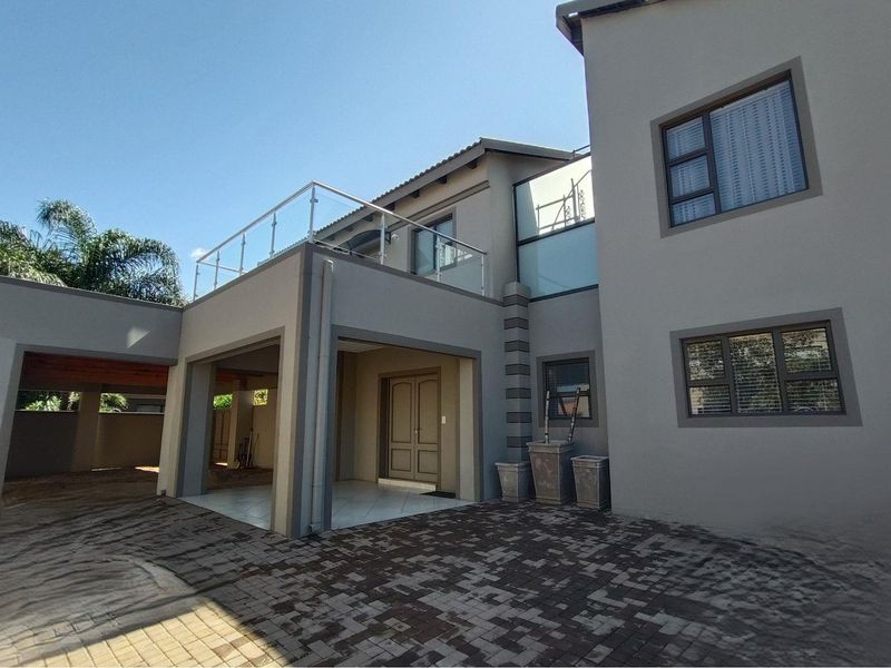 A modern double-story residential exterior featuring a paved driveway, covered entrance porch, and an upper-level balcony with glass balustrades.
