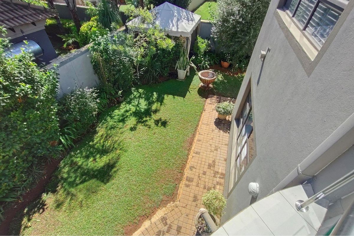 An elevated view of the private rear garden featuring a paved walkway, lush lawn, and established perimeter walling.
