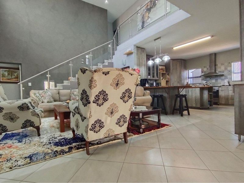 Spacious open-plan living area featuring a modern kitchen with breakfast bar, tiled flooring, and a staircase with glass balustrade leading to the upper level.