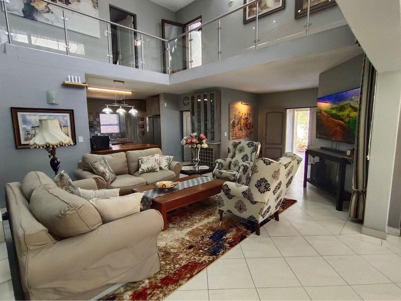 Spacious open-plan living area featuring a double-volume ceiling, glass balustrade mezzanine, tiled flooring, and integrated kitchen access.