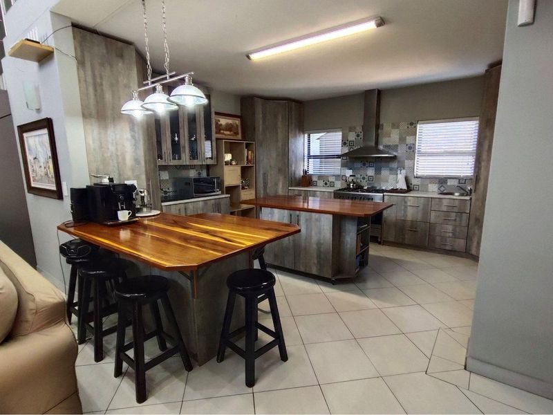 Modern open-plan kitchen featuring wood-look cabinetry, a central island with a timber countertop, tiled flooring, and a stainless steel extractor fan.