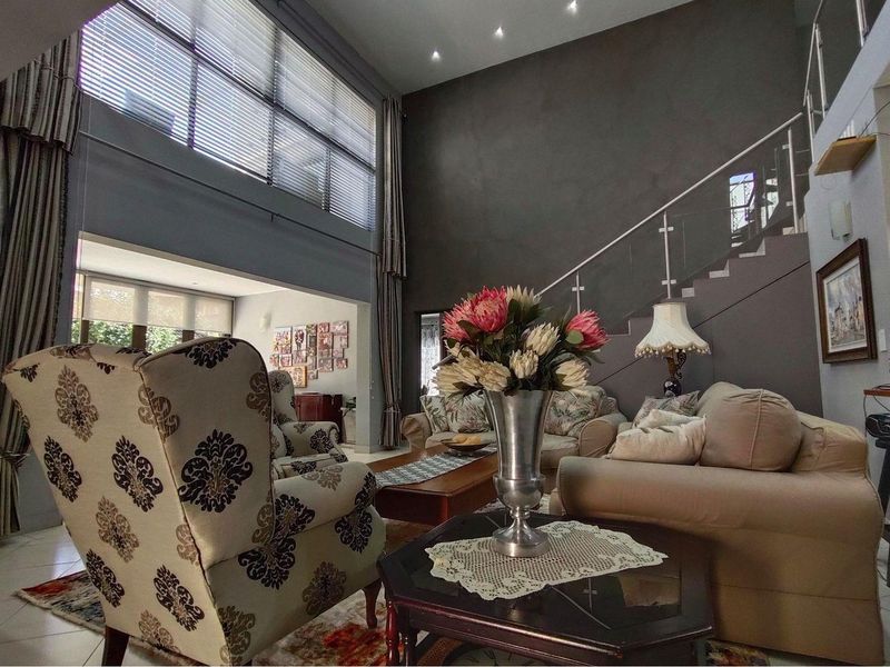 Spacious double-volume living area featuring high ceilings, large windows, tiled flooring, and a modern staircase with glass balustrades.