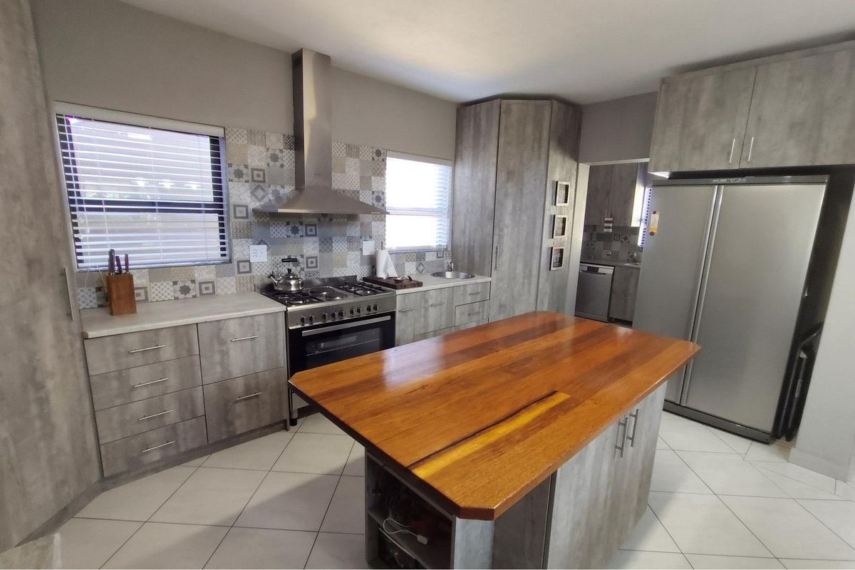 Modern kitchen featuring grey cabinetry, a wooden island countertop, stainless steel gas stove with extractor fan, and decorative tiled backsplash.