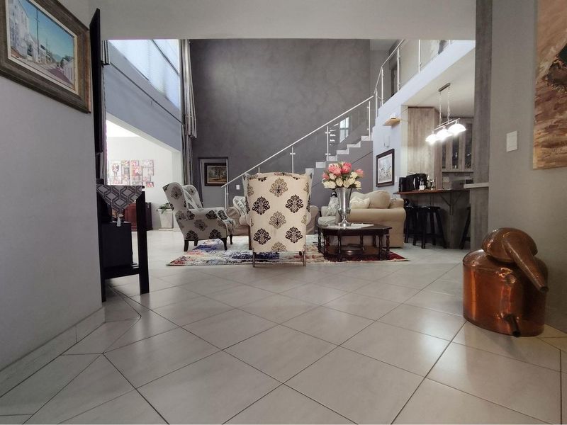 Spacious open-plan living area featuring high ceilings, tiled flooring, a modern staircase with glass balustrades, and an integrated kitchen breakfast bar.