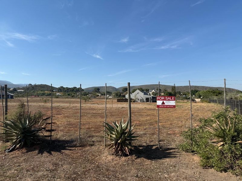 A vacant residential plot featuring perimeter wire fencing, established aloe plants, and scenic mountain views, currently available for sale.