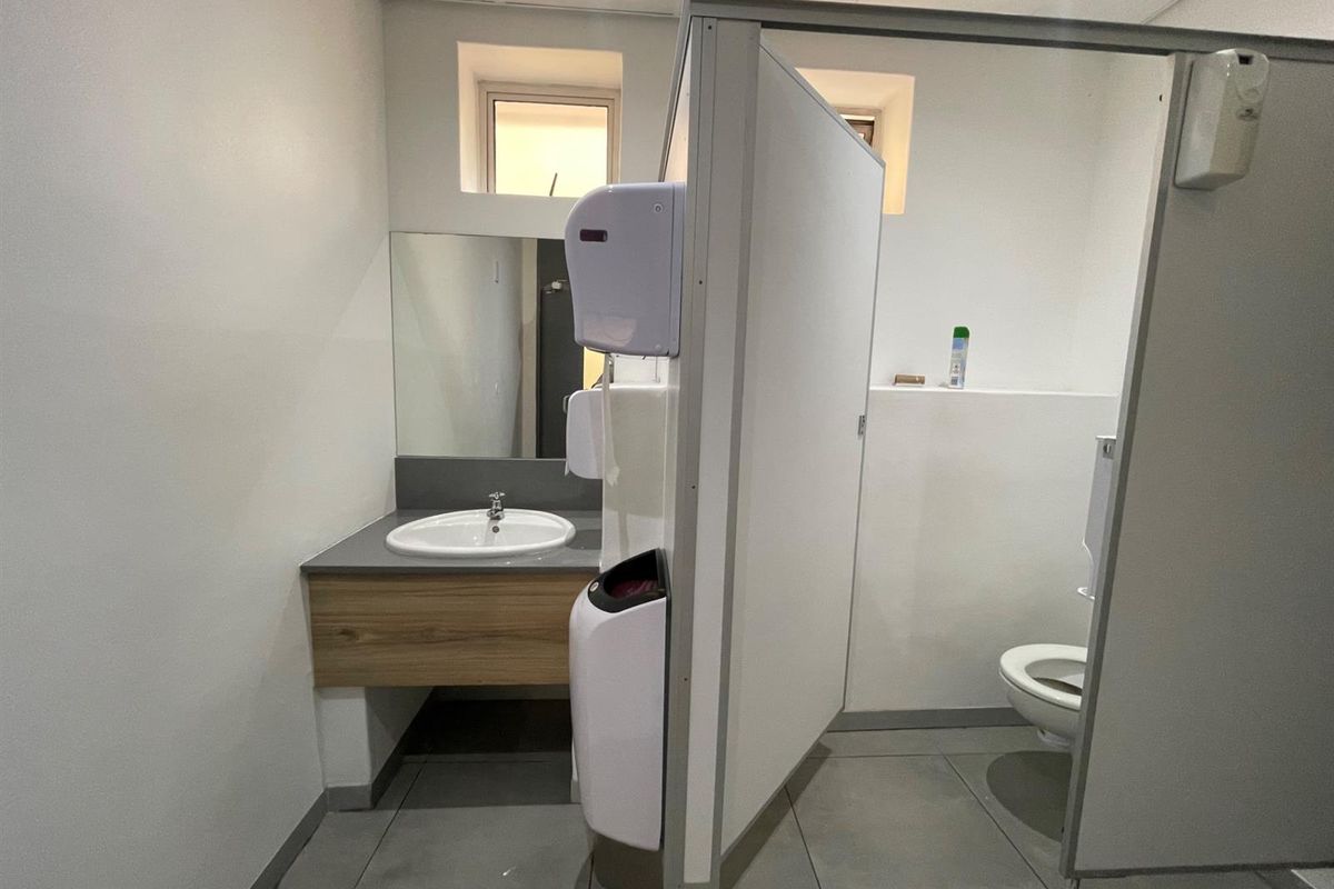 A functional office bathroom featuring a vanity with integrated sink, wall-mounted mirror, and a private toilet stall with partition.