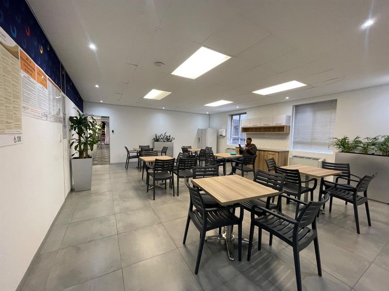 A spacious office breakroom or canteen area featuring tiled flooring, recessed lighting, and built-in cabinetry with a neutral, professional finish.