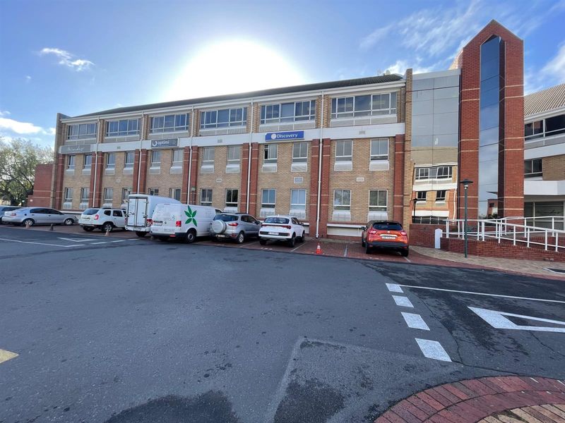 Front elevation of a multi-story commercial office building featuring brick cladding, large windows, and an adjacent paved parking lot.