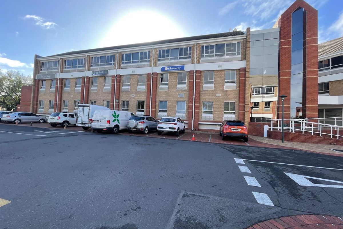 Front elevation of a multi-story commercial office building featuring brick cladding, large windows, and an adjacent paved parking lot.