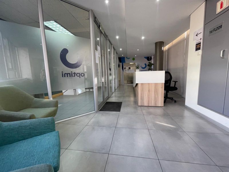 Modern office reception area featuring a built-in reception desk, glass partition walls, and clean tiled flooring with recessed lighting.