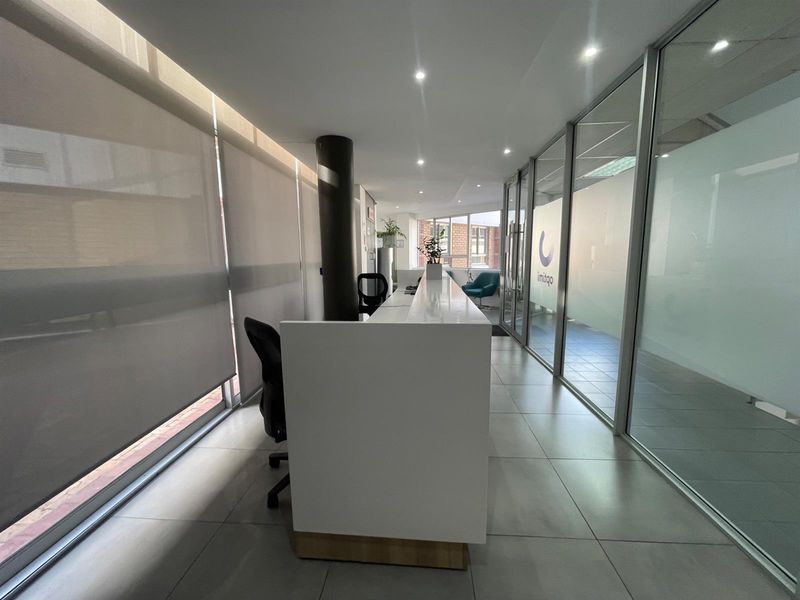 Modern office reception area featuring a built-in desk, glass partition walls, tiled flooring, and recessed lighting.