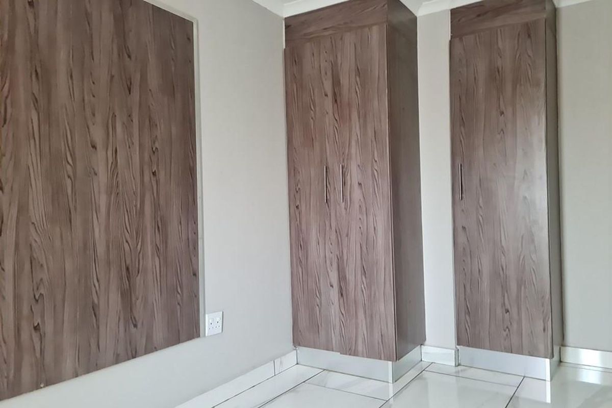 A bedroom featuring built-in wood-grain cabinetry and polished white floor tiles, offering clean lines and modern storage solutions.