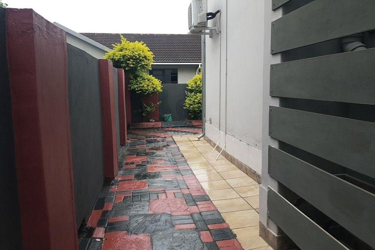 A side walkway featuring patterned paving, tiled flooring, and a wall-mounted air conditioning unit, leading towards the rear of the townhouse property.