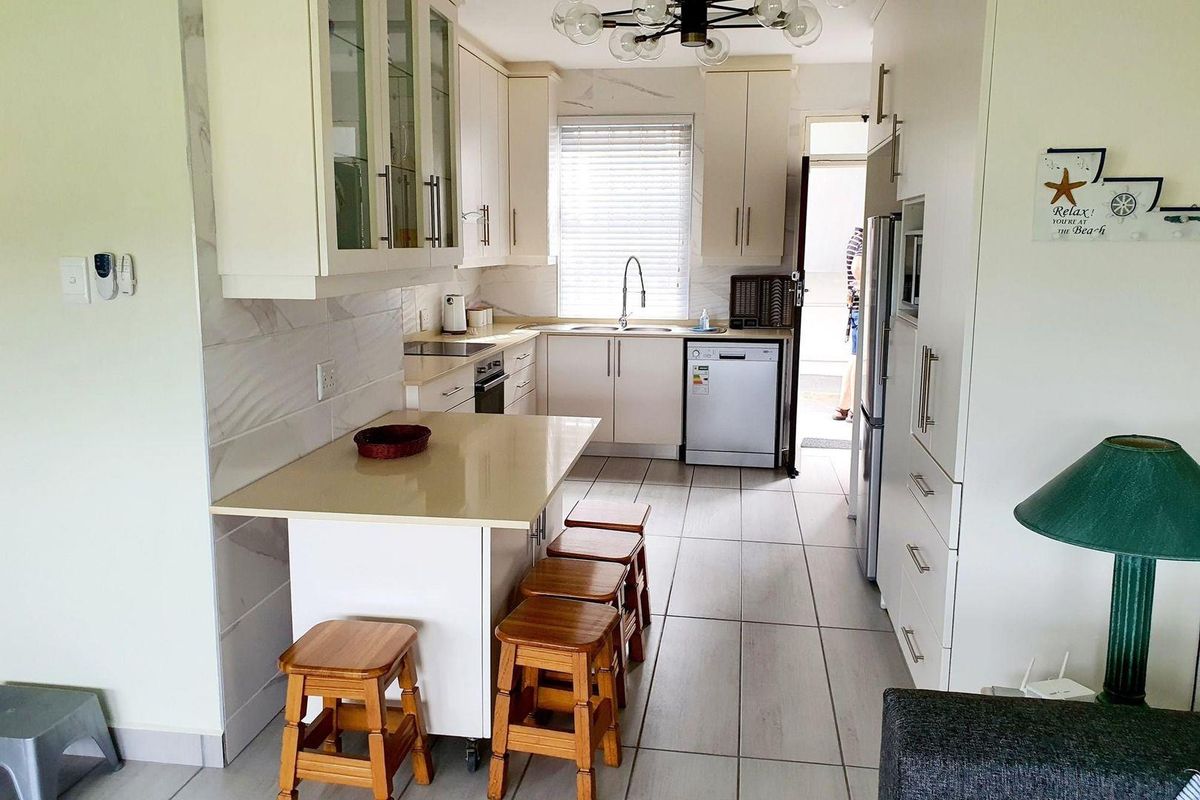 A functional kitchen featuring light-toned cabinetry, stone-look countertops, a breakfast bar, and tiled flooring, offering a clean and practical layout.