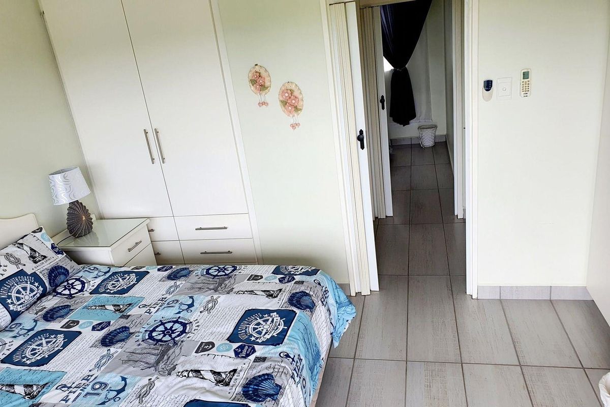 A bedroom featuring built-in cupboards and tiled flooring, with an adjacent hallway leading to another area of the apartment.