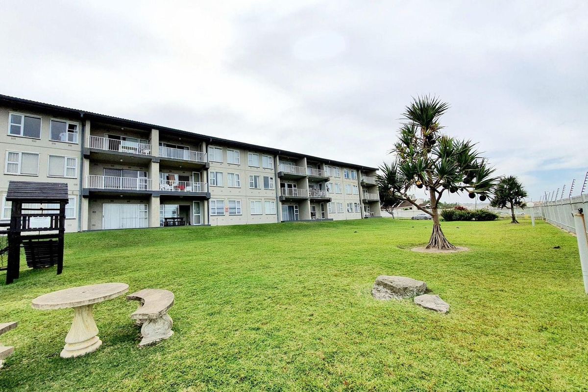 Exterior view of the apartment complex featuring a large communal lawn area, established trees, and private balconies for each unit.
