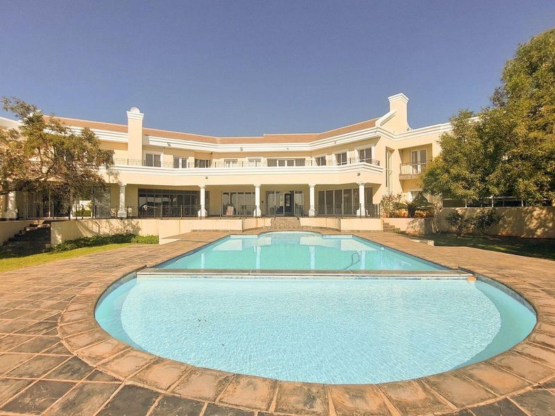 Spacious rear exterior featuring a large swimming pool with stone decking, overlooking a grand two-story residence with a covered patio and upper balcony.