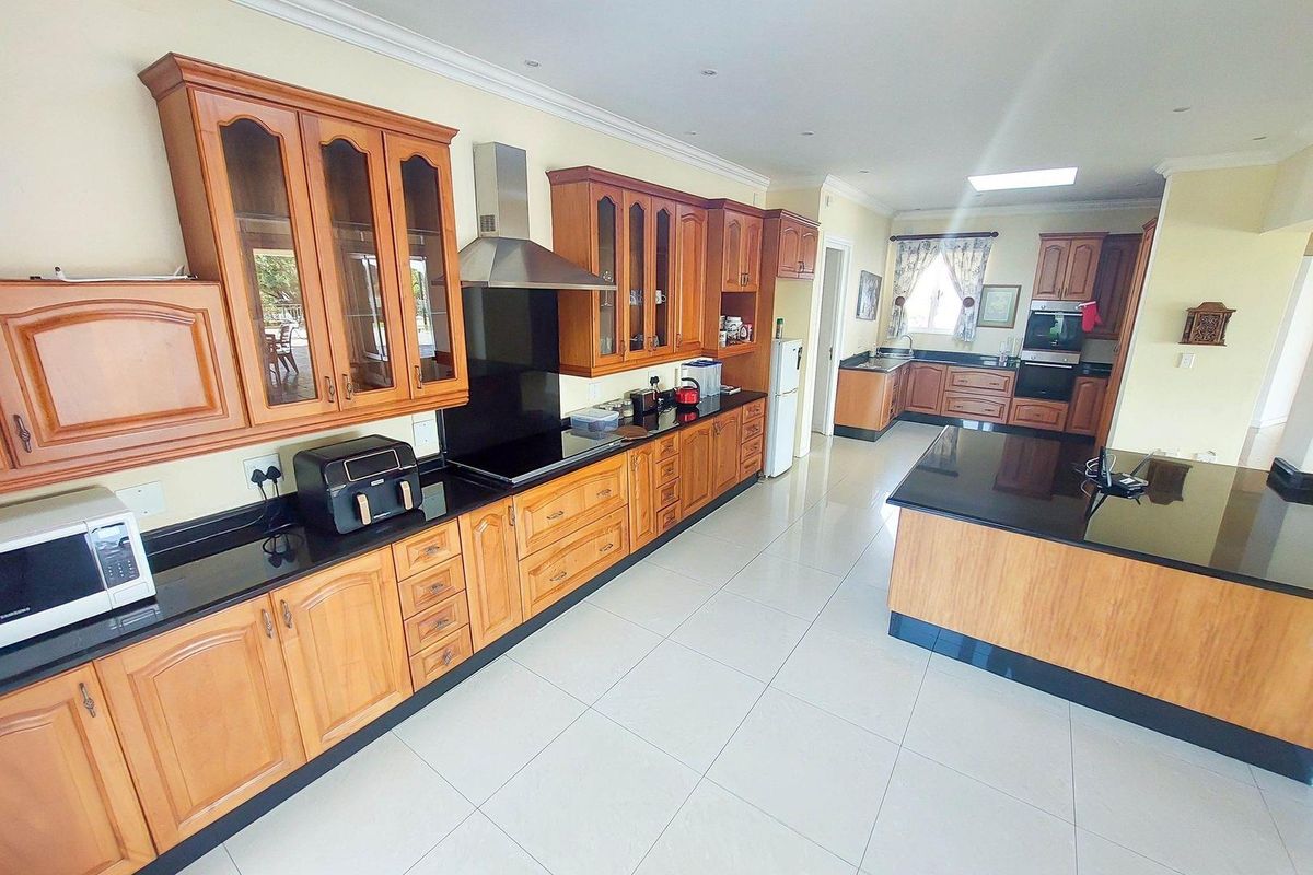 Spacious kitchen featuring wooden cabinetry, granite countertops, a central island, and built-in appliances with tiled flooring throughout.