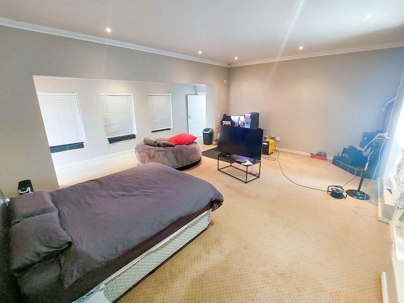 Spacious bedroom featuring neutral wall tones, recessed downlighting, coving, and multiple windows with fitted venetian blinds.