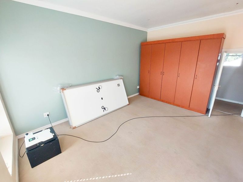 A spacious bedroom featuring neutral carpeted flooring, built-in wooden cupboards, and a soft green accent wall.