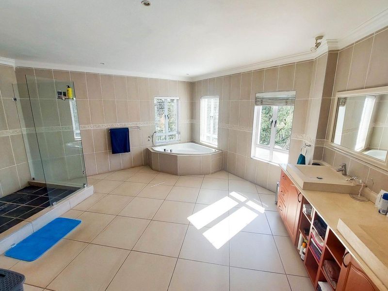 Spacious bathroom featuring a corner bathtub, glass-enclosed shower, and double vanity with ample built-in storage and natural light.