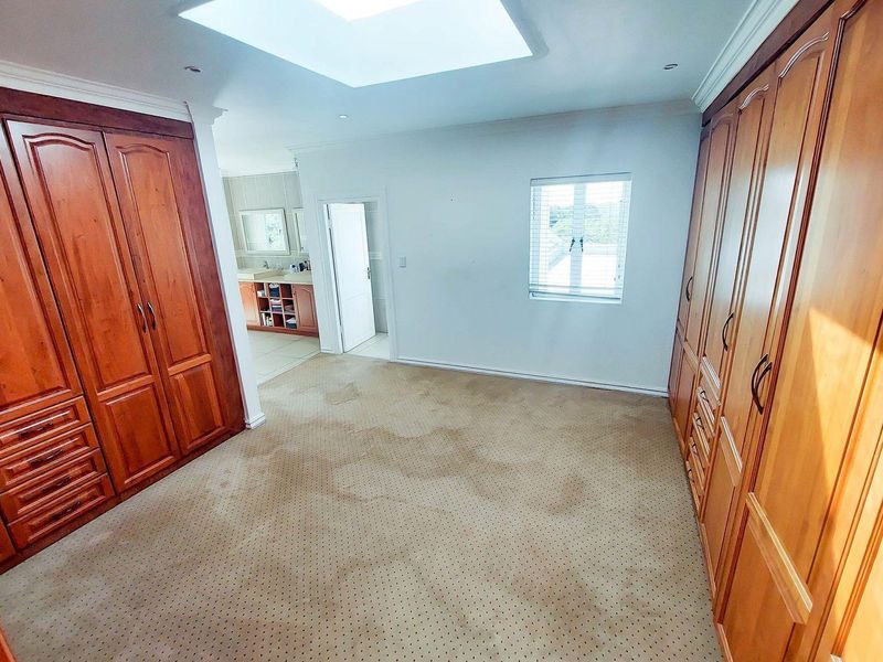 Spacious bedroom featuring extensive built-in wooden cabinetry, a skylight for natural light, and direct access to an en-suite bathroom.