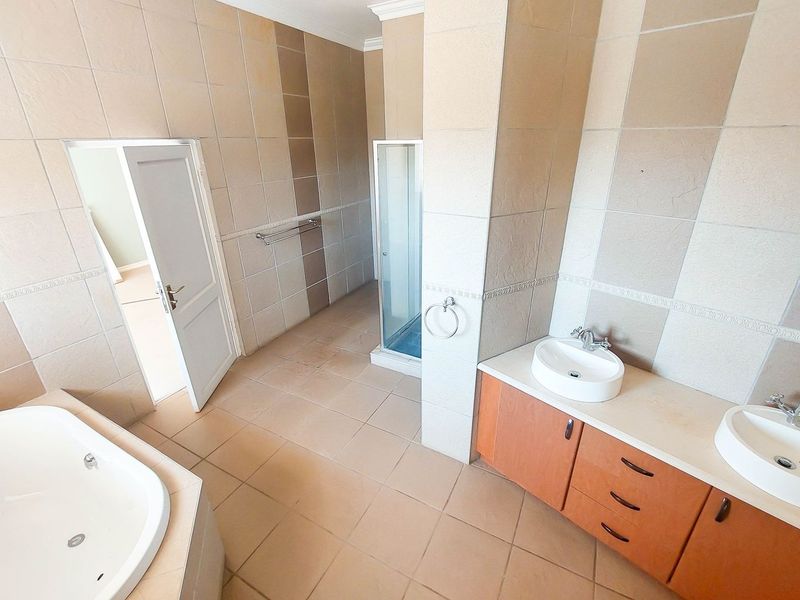 Spacious bathroom featuring a double vanity with vessel sinks, a built-in bathtub, and a separate shower enclosure with neutral tiled finishes.