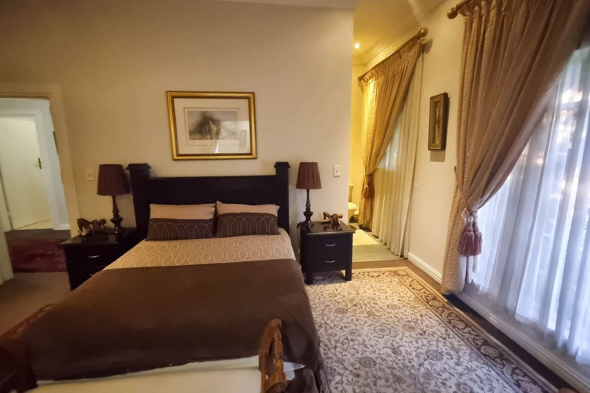 A well-maintained bedroom featuring neutral walls, classic window treatments, and an adjoining en-suite bathroom area.