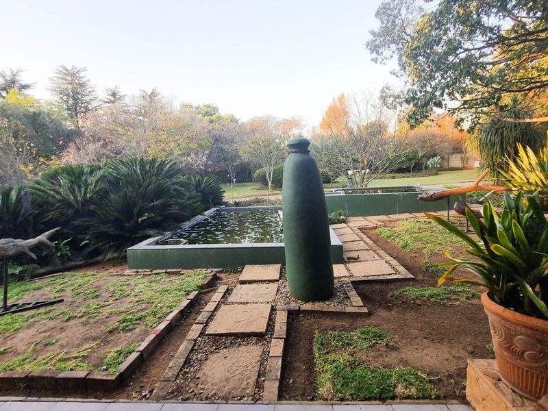 A landscaped garden area featuring a raised rectangular water feature, stone paver pathways, and established shrubbery in a tranquil outdoor setting.