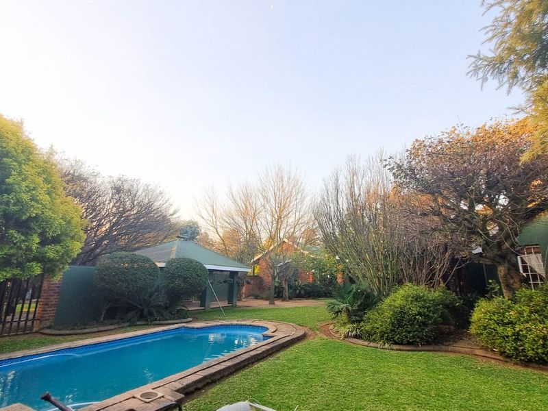 A spacious backyard featuring a swimming pool, established garden landscaping, and a covered outdoor entertainment area.