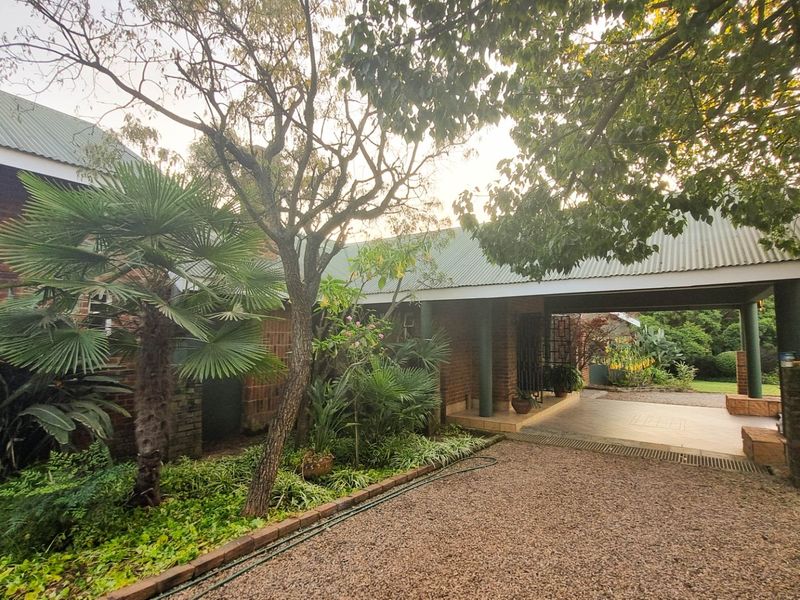A view of the front exterior featuring a brick facade, covered entrance area, and established garden with a gravel driveway.