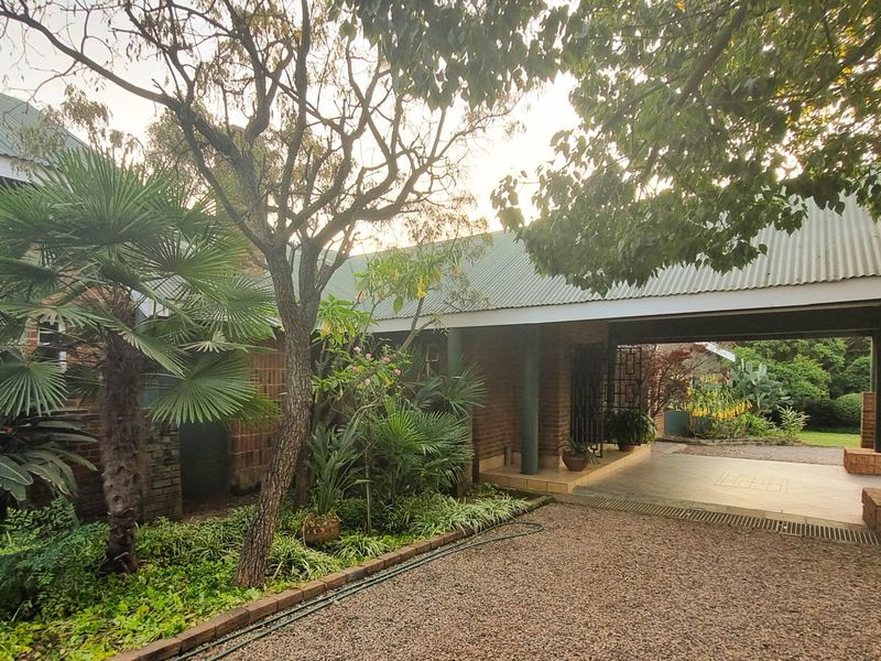 A view of the property's front exterior, featuring a covered patio area, brick facade, and established garden landscaping.