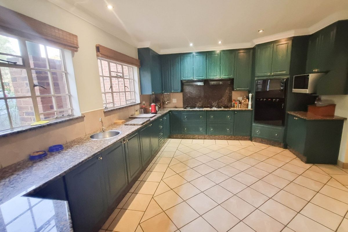 Spacious kitchen featuring dark green cabinetry, granite countertops, integrated oven, built-in microwave, and tiled flooring with ample natural light from large windows.