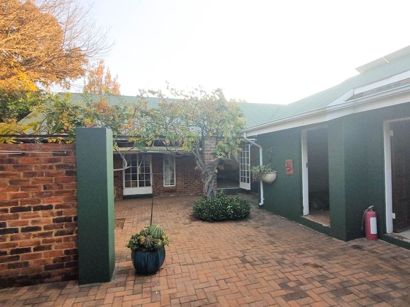 A paved rear courtyard area featuring brick walls, established trees, and direct access to the main dwelling.